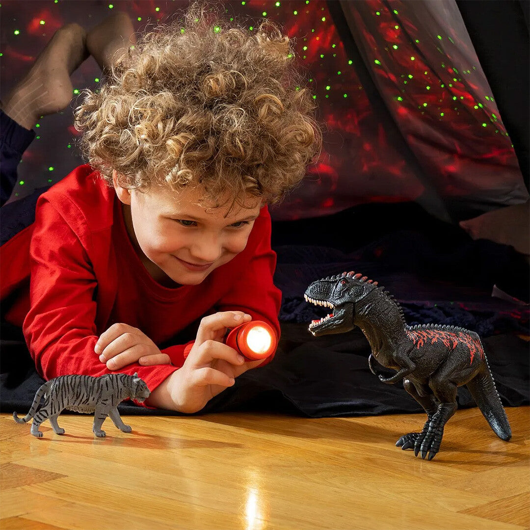 Kind speelt met een Schleich Giganotosaurus dinosaurusfiguur en een tijgerfiguur in een donkere tent.