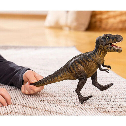 Een kinderhand houdt het Schleich Tarbosaurus dinosaurus speelgoedfiguur vast op een vloerkleed.