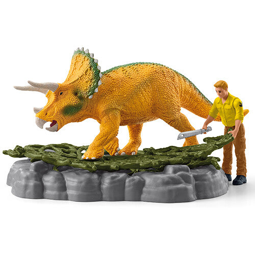 Schleich triceratops figuur op een plantenbasis met een mannelijke figuur die een zaag vasthoudt.
