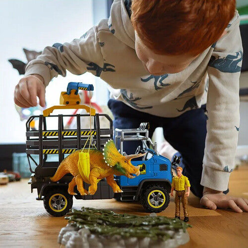 Kind speelt met de Schleich dinosaurusspeelset, waarbij een triceratops met een kraan op een truck wordt gehesen.