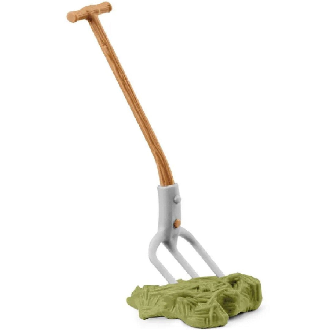 Een detailfoto van een Schleich boerderij speelgoed hooivork die in een hoopje hooi steekt.