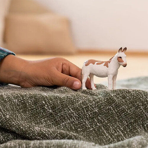 Een kinderspeelgoedfiguurtje van een gevlekte ezel op een deken, met een kinderhand ernaast.