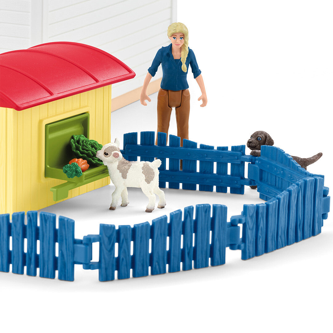 Detail van de Schleich dierenhotel speelset met een mensfiguur, een geitje, een hond en een voederstation met blauwe hekjes.