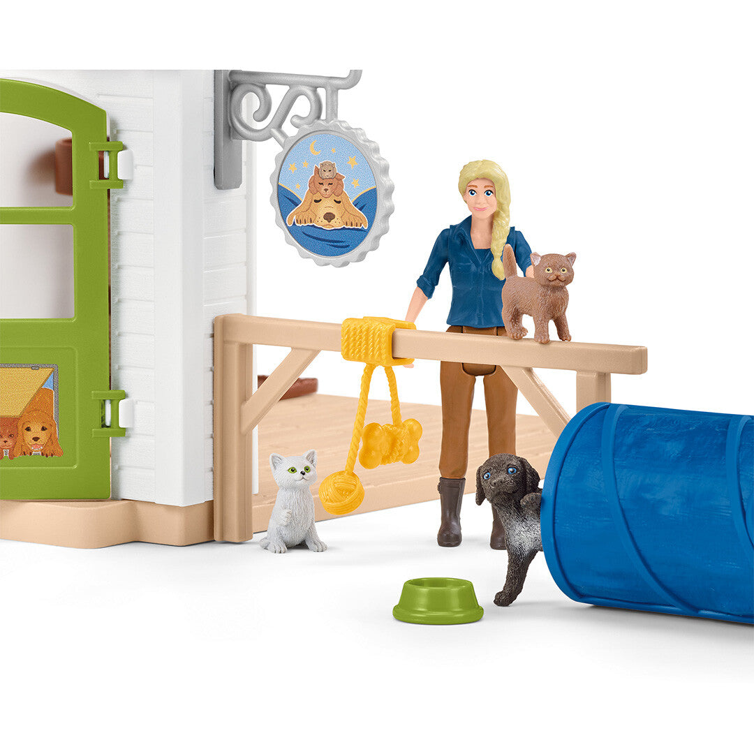 Detail van de Schleich dierenhotel speelset met een mensfiguur, twee katten, een hond en een blauwe tunnel bij de ingang van het huis.