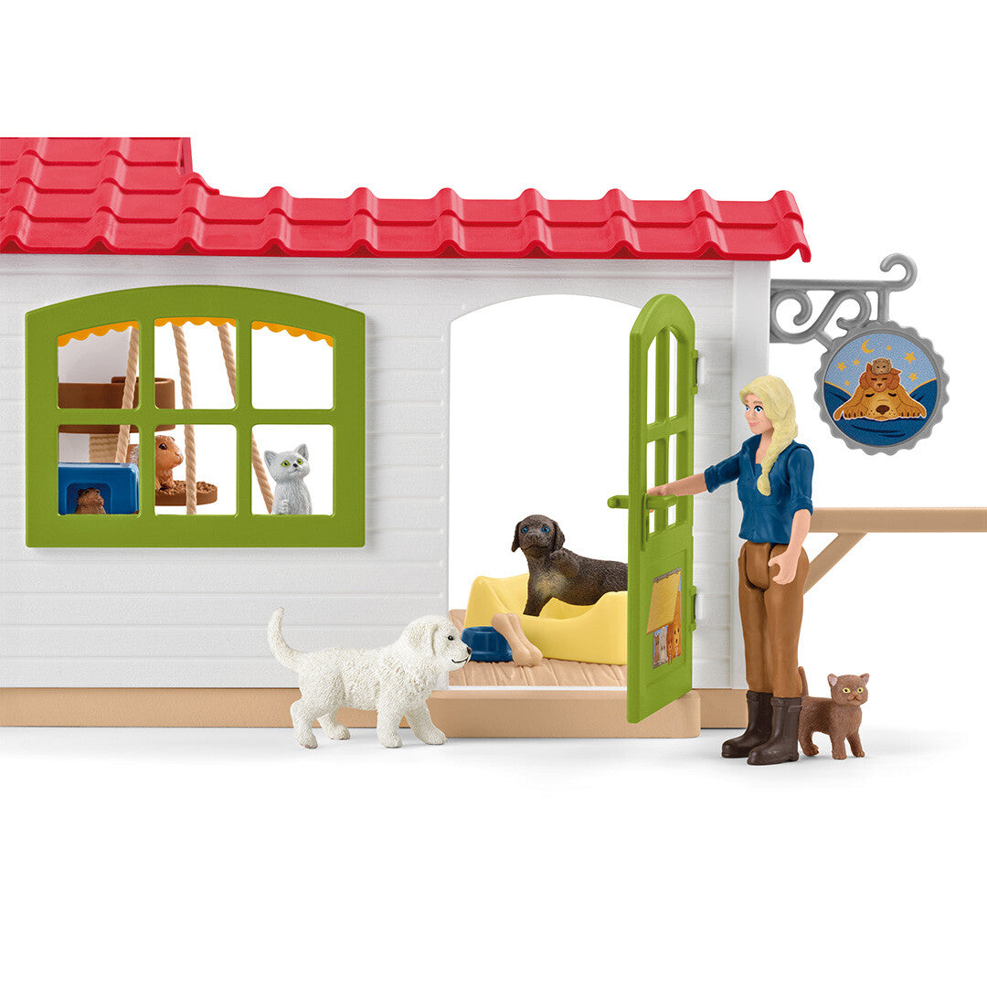 Detail van de Schleich dierenhotel speelset met een mensfiguur die de deur van het huis opent, met honden en een kat.