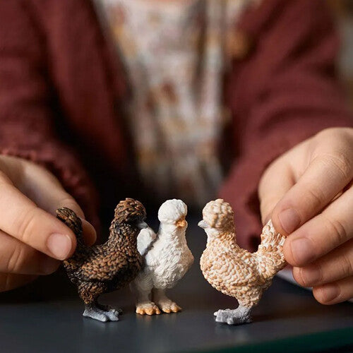 Kinderhanden spelen met de drie schleich kippen dierenfiguurtjes.