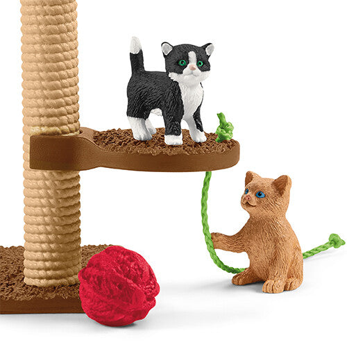 Close-up van een Schleich krabpaal met een zwart-witte kat en een bruine kat die met een touwtje speelt.