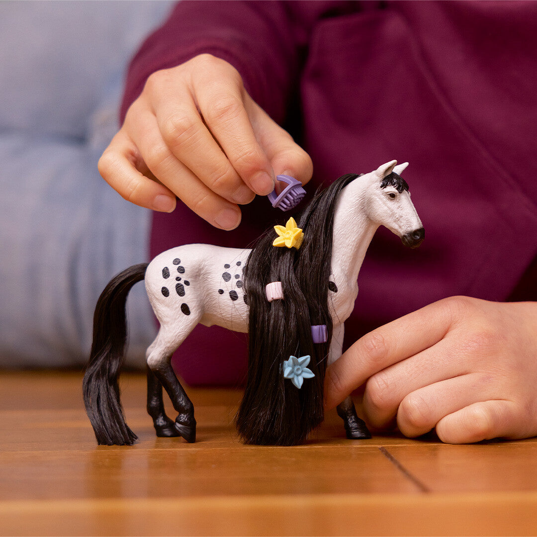 Een kind kamt de lange zwarte manen van de schleich Knabstrupper hengst speelgoedfiguur met een paarse kam.