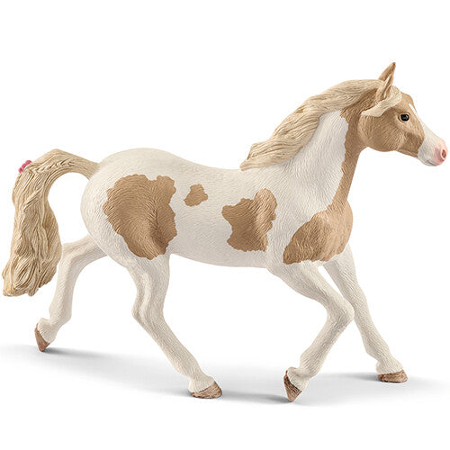 Schleich dierenfiguurtje van een witte paint merrie met bruine vlekken en een roze strik in de staart.