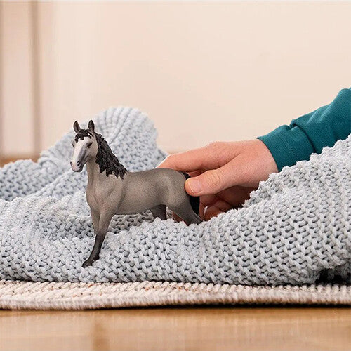 Een Schleich Selle Français merrie dierenfiguurtje op een gebreide deken, aangeraakt door een kinderhand.