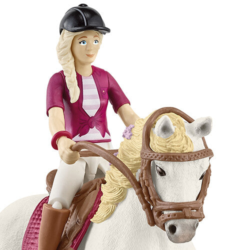 Detail van de Schleich speelgoedfiguur van een meisje met zwarte cap en blond haar op een wit paard.