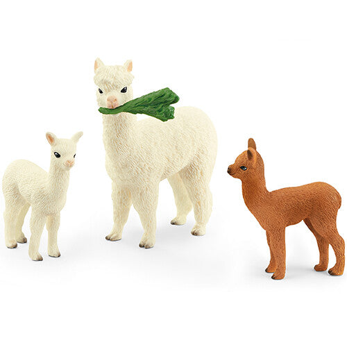 Schleich dierenfiguurtjes van een witte alpaca met een groen blad in de mond en twee veulens, één wit en één bruin.