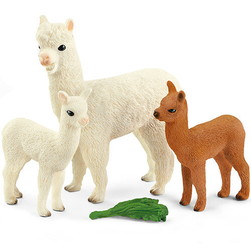 Schleich dierenfiguurtjes van een witte alpaca met twee veulens, één wit en één bruin, en een los groen blad op de grond.