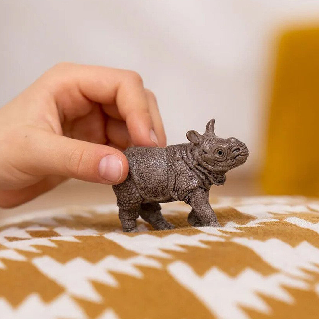 Een hand houdt het Schleich Indisch neushoornkalf dierenfiguurtje vast op een deken.
