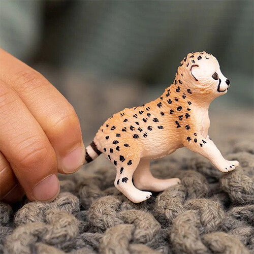 Schleich jachtluipaardwelp dierenfiguurtje van plastic, vastgehouden door een hand op een gebreide ondergrond.
