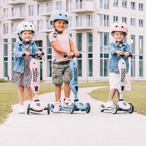 Drie kinderen met helmen staan met hun Scoot & Ride 2-in-1 steps in roze en blauw op een pad.