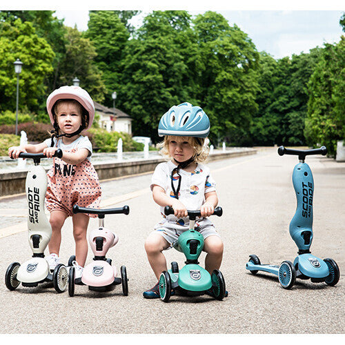 Drie kinderen met verschillende kleuren Scoot & Ride Highwaykick 1 2-in-1 loopfietsen en steps in een park.
