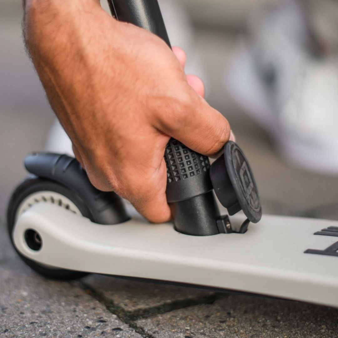 Een hand die een onderdeel van de beige Scoot & Ride 2-in-1 step vasthoudt.