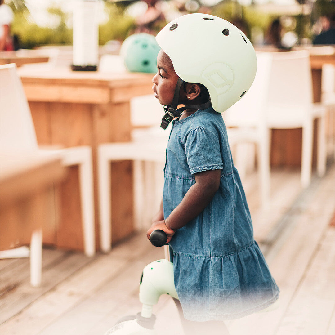 Een kind met een lichtgroene kinderhelm op, gezien vanaf de zijkant, rijdend op een loopfiets.