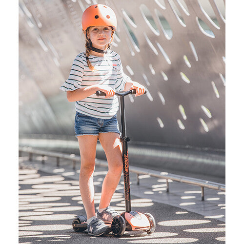 Meisje met oranje helm rijdt op een peachkleurige Scoot & Ride kinderstep Highwaykick 5 buiten.