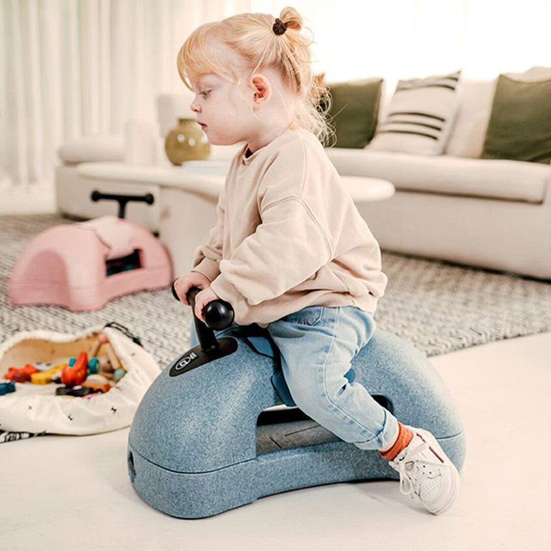 Een peuter zit op de blauwe Scoot & Ride foam loopwagen in een woonkamer.