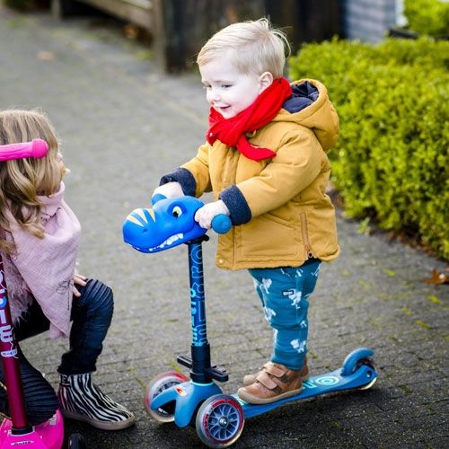 Een kind rijdt op een blauwe scooter met een Scootaheadz blauw dinohoofd accessoire.