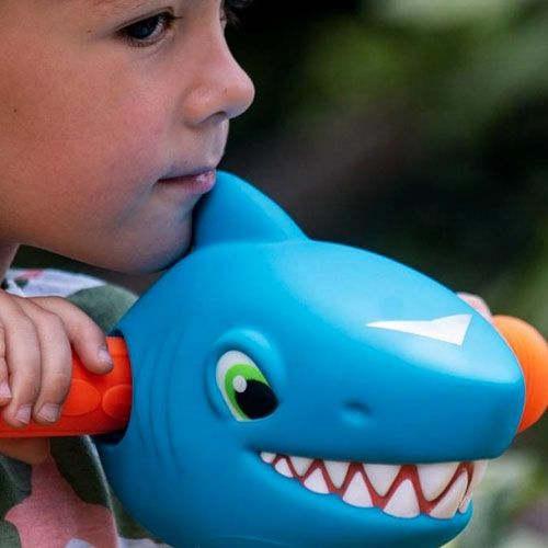 Kind met oranje handvatten naast een blauwe Scootaheadz haaienhoofd accessoire op een kinderstep.