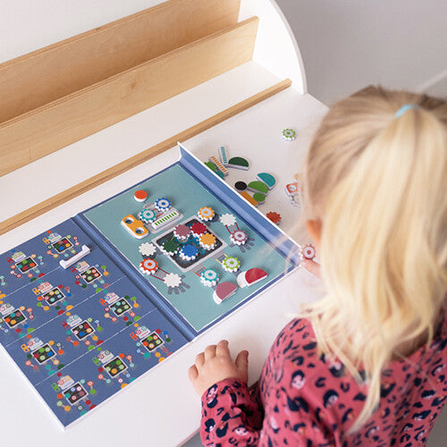 Een kind speelt met het open Scratch Europe magneetboek Edulogic, waarbij ze magnetische robotonderdelen plaatst op een witte tafel.