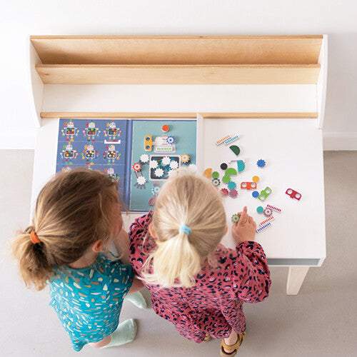 Twee kinderen spelen van bovenaf gezien met het open Scratch Europe magneetboek Edulogic met robotthema op een witte tafel.