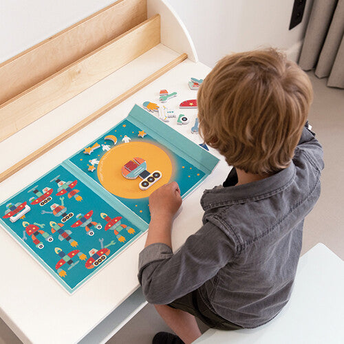 Een kind zit aan een bureau en speelt met het Scratch Europe magnetisch speelboek met ruimtefiguren.