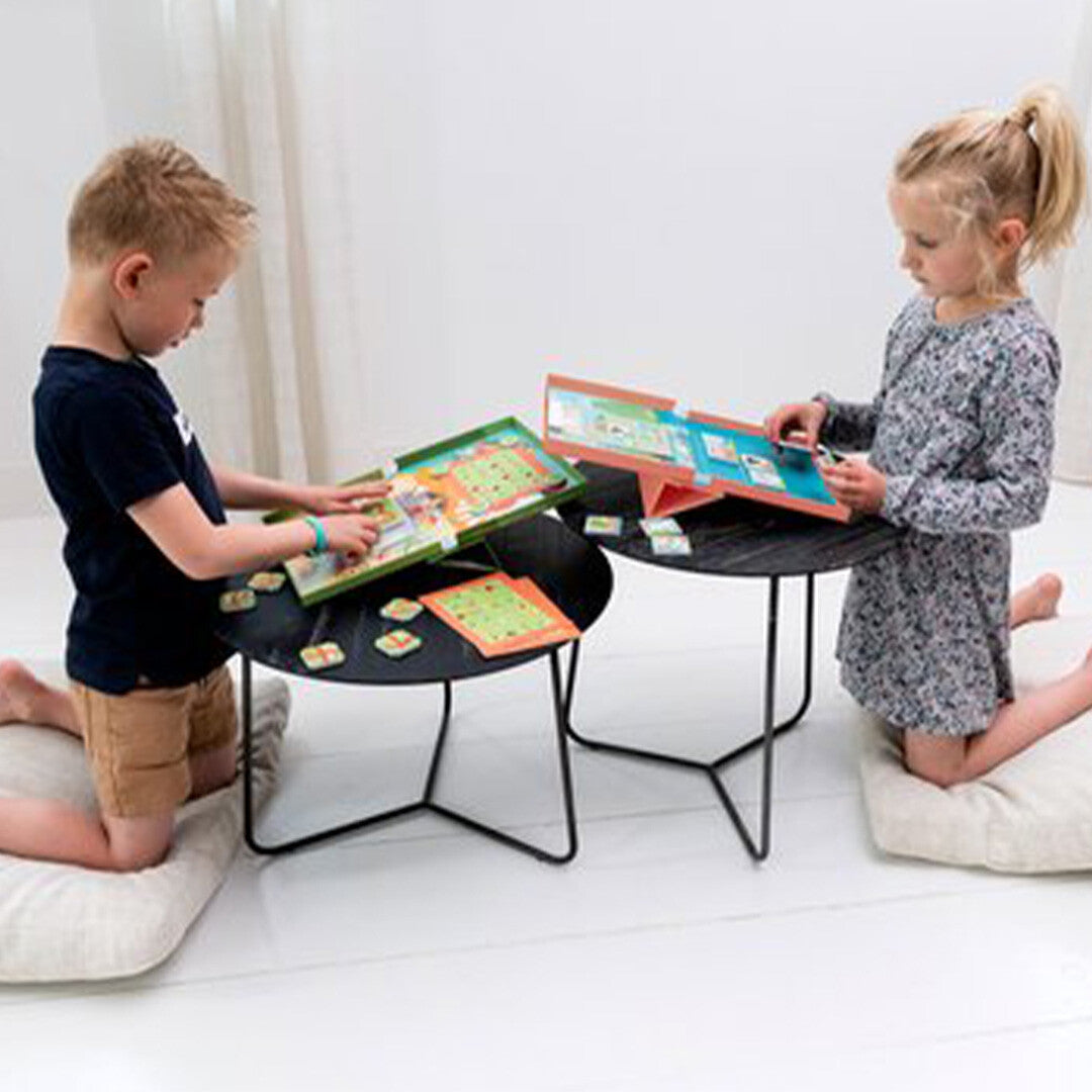 Twee kinderen spelen met het Scratch Europe magnetisch doolhofspel, zittend op kussens aan kleine tafels.