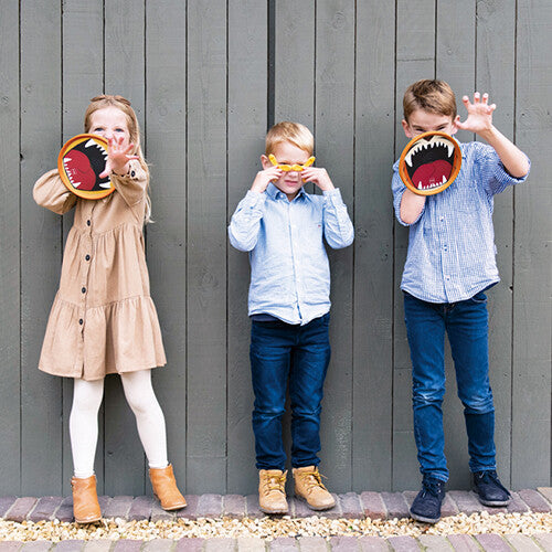 Drie kinderen poseren met de oranje vangschijven met tijger/leeuwenmonden en de gele boemerang van het vangspel.