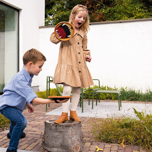 Twee kinderen spelen buiten met het vangspel, waarbij een meisje een oranje vangschijf vasthoudt en een jongen klaarstaat om te gooien.