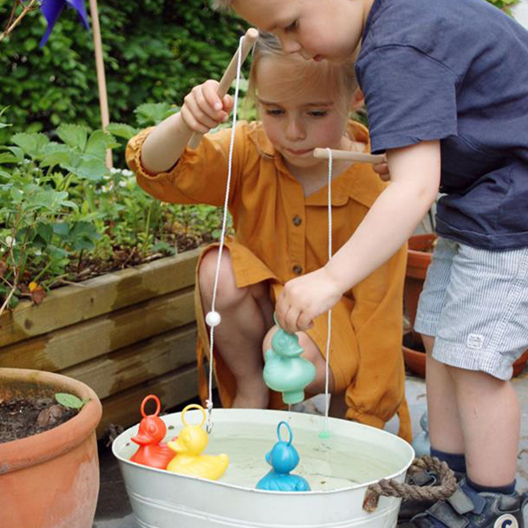 Twee kinderen vissen samen op gekleurde eendjes in een witte teil buiten.