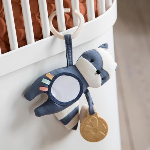 Sebra activiteitenknuffel wasbeer hangend aan een wit babybedje.