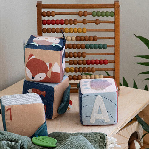 Drie Sebra zachte babyblokken met bosdieren, letters en cijfers op een houten plank, met een telraam op de achtergrond.