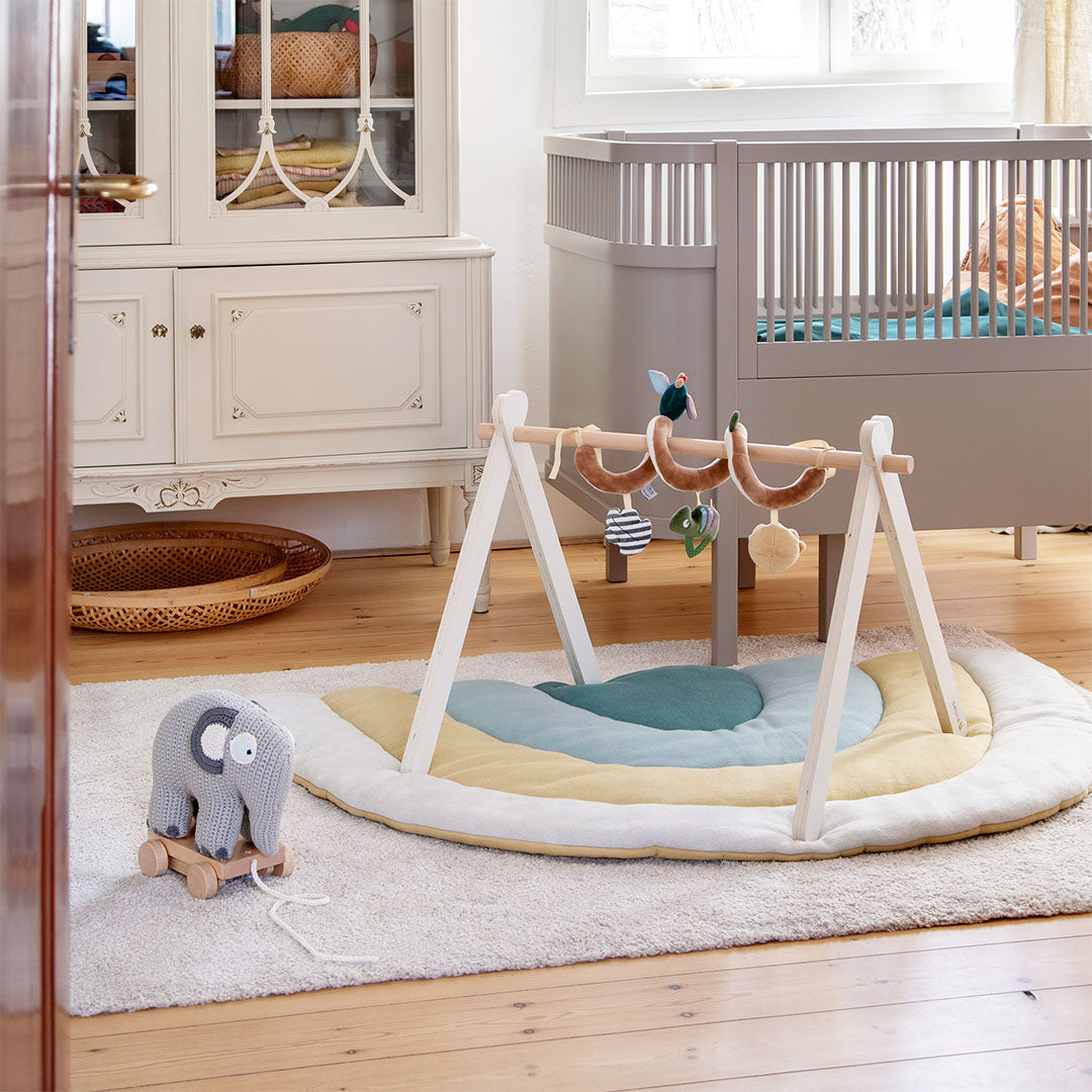 Sebra houten babygym met hangende speeltjes boven een speelkleed in een babykamer.