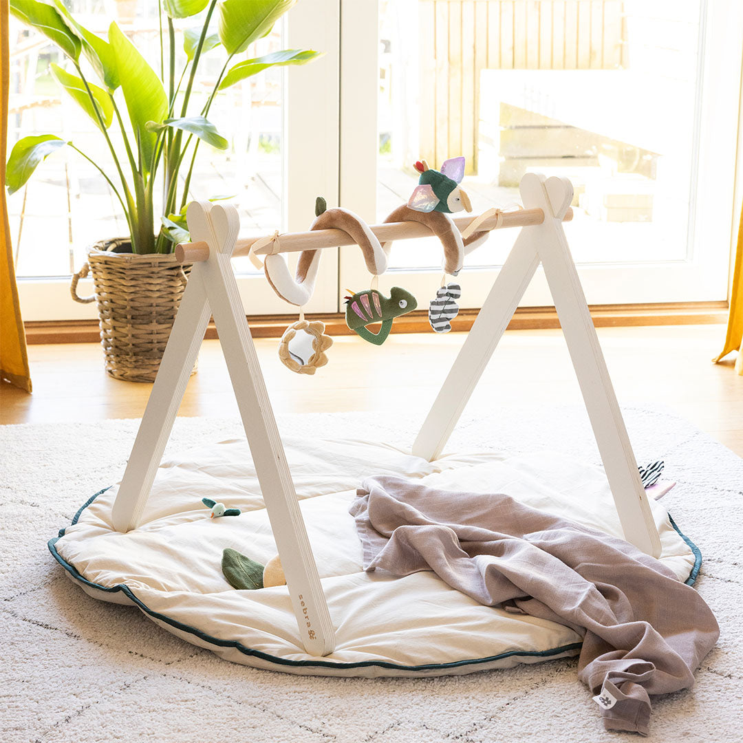 Sebra houten babygym met diverse hangende speeltjes boven een crèmekleurig speelkleed.