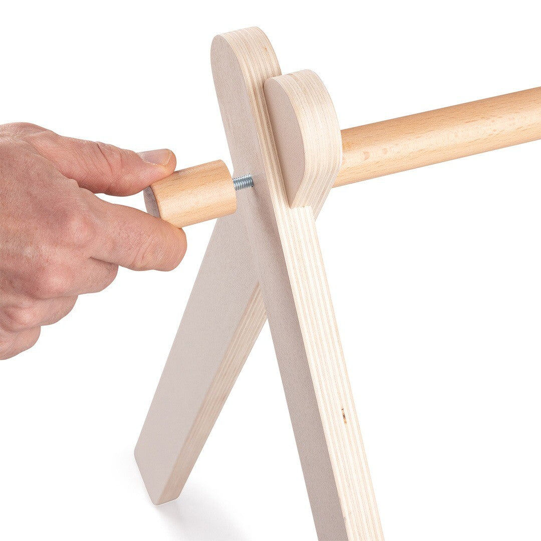 Detail van een hand die een houten knop bevestigt aan het frame van de babygym.