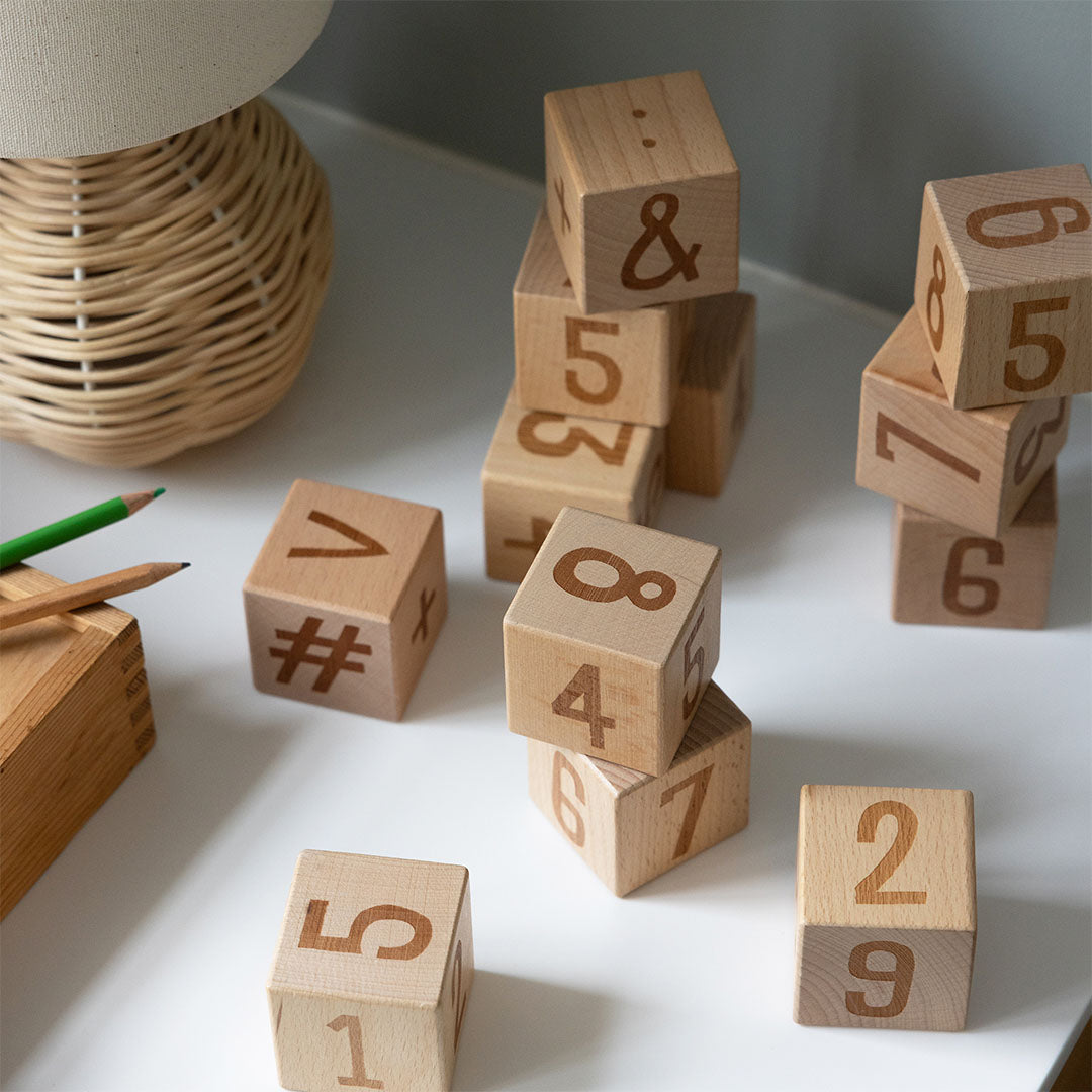 Sebra houten educatieve blokken met nummers en symbolen, liggend op een tafel naast een lamp.