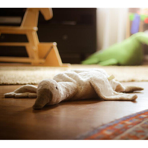 Senger witte pluchen warmteknuffel gans ligt op een houten vloer.