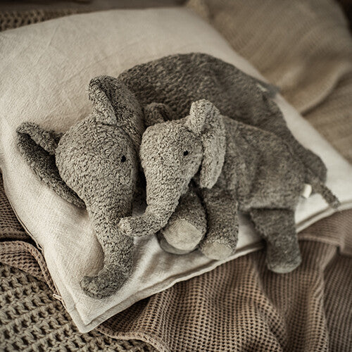 Twee Senger warmteknuffel olifanten van grijs pluche, een grote en een kleine, liggen op een kussen op bed.