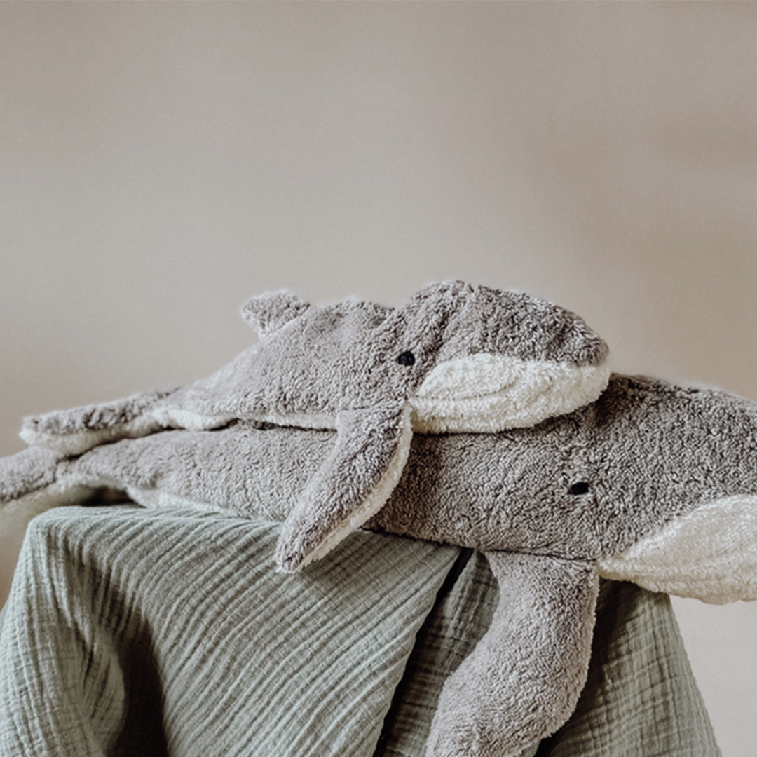 Twee Senger pluchen warmteknuffels in de vorm van grijze walvissen, een grote en een kleine, liggen op een groene doek.