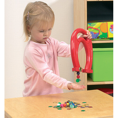 Een jong kind gebruikt de Shaw magnets rode hoefijzermagneet om gekleurde magnetische fiches op te pakken.