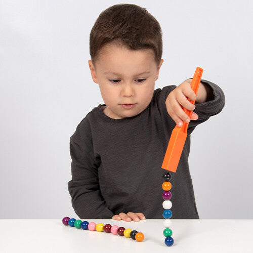 Een kind pakt met een oranje magneetstaaf Shaw Magnets magnetische knikkers op, die een ketting vormen.