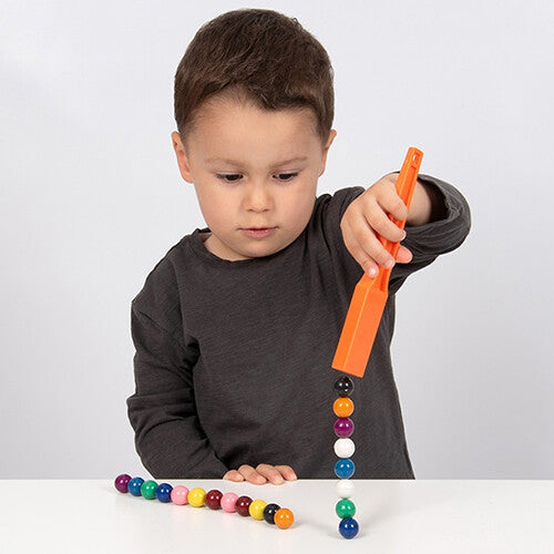 Een kind speelt met Shaw Magnets educatief speelgoed, waarbij hij met een oranje magneetstaaf een verticale stapel kleurrijke magnetische knikkers optilt.