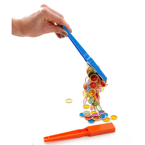 Een hand houdt een blauwe magneetstaaf vast die kleurrijke magnetische schijfjes laat vallen op een oranje magneetstaaf.