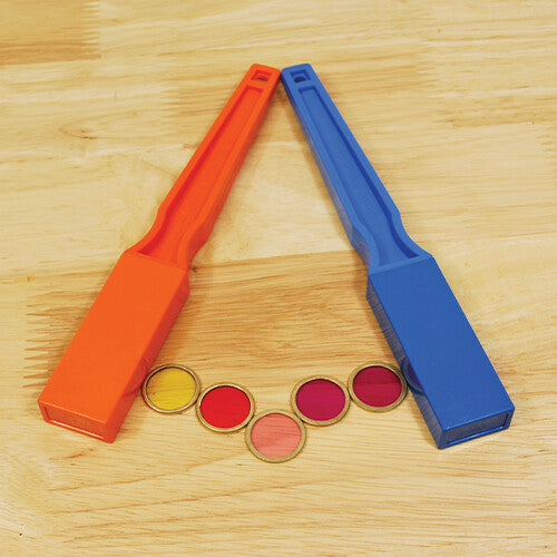 Twee magneetstaven, oranje en blauw, liggen in een V-vorm met vijf kleurrijke magnetische schijfjes ertussen op een houten tafel.