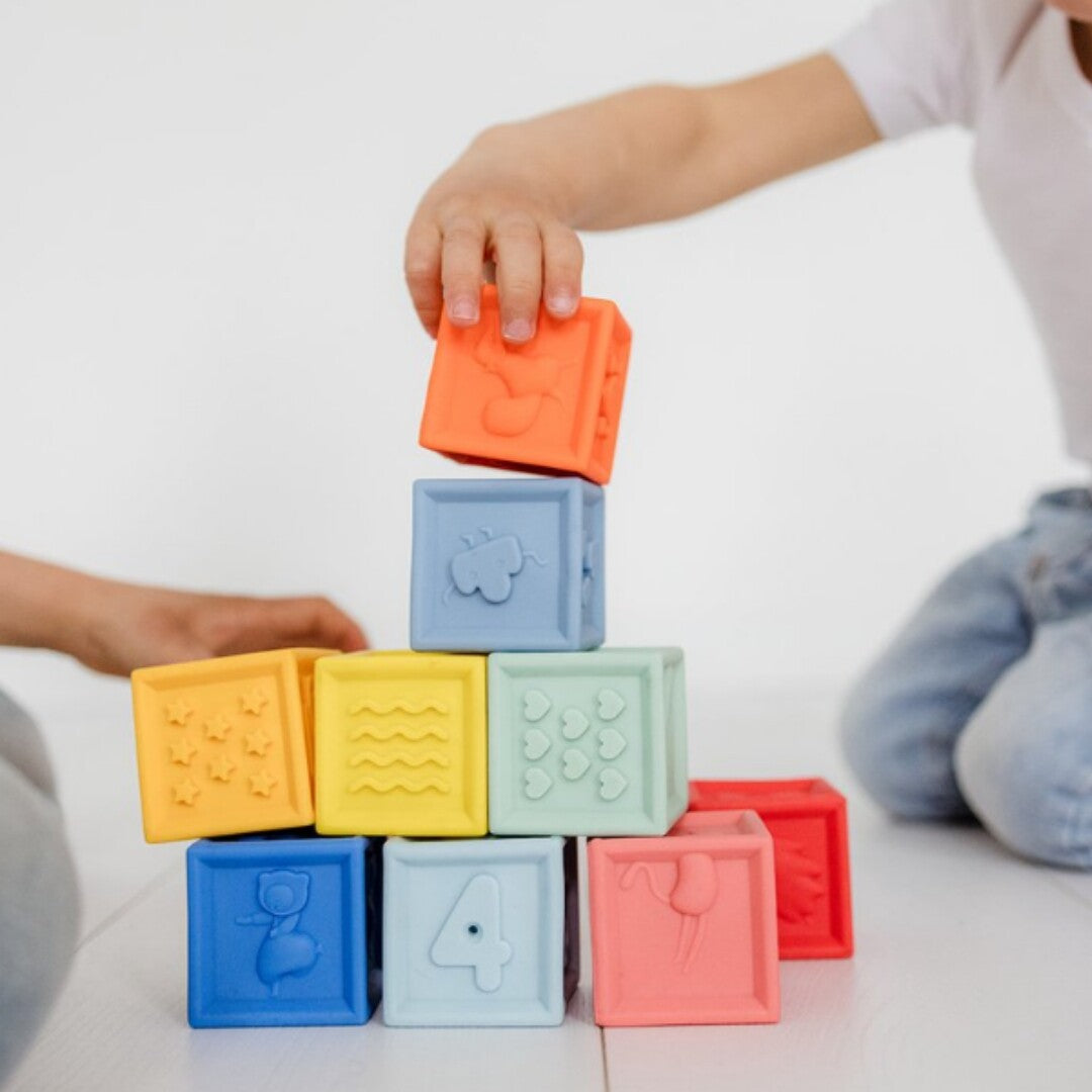 Een kind stapelt kleurrijke zachte stapelblokken met cijfers en figuren.
