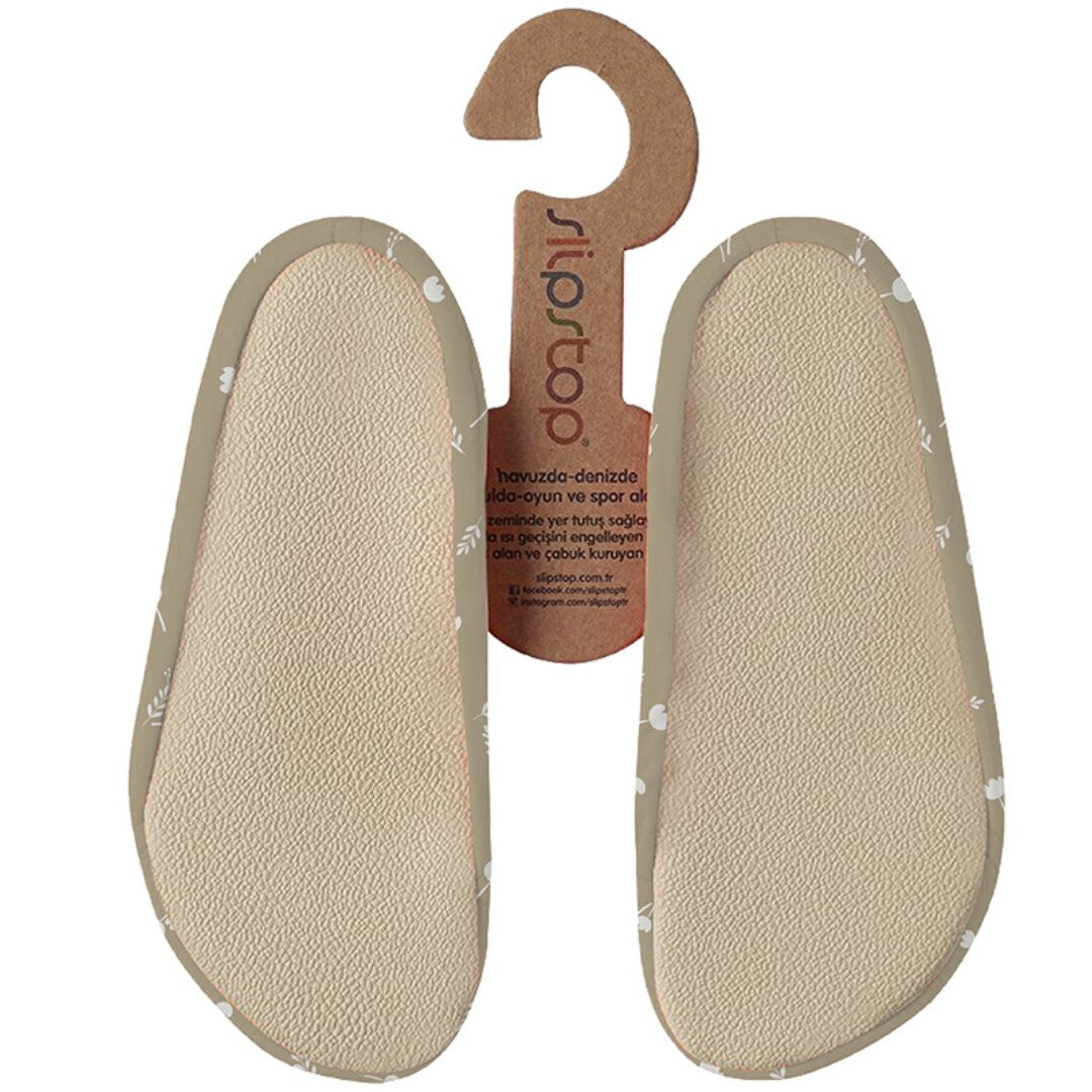 De onderkant van Slipstop baby- en peutersportschoenen in beige met wit bloemenpatroon, aan een kartonnen hanger.